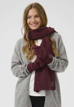 Burgunderfarbener Strickschal kombiniert mit passenden Handschuhen. Der Schal hat eine gerippte Textur; die Handschuhe sind im Design tailliert und haben einen strukturierten Bund.
