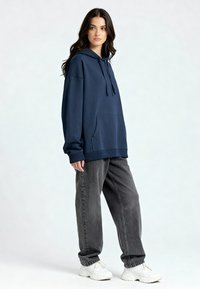 Felpa con cappuccio blu navy con tasca frontale, polsini e orlo a coste, abbinata a jeans grigi a taglio morbido e sneaker bianche. Tessuto dalla trama liscia.