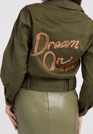 Chaqueta verde oliva con texto bordado en naranja "Dream On" en la espalda, combinada con una falda verde oliva a juego, vista desde atrás.