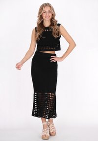 Černý pletený dvoudílný outfit skládající se z cropped topu s výřezy a dlouhé sukně s rozparkem a otevřeným vzorem.