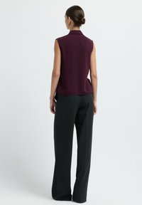 Blusa senza maniche di colore bordeaux realizzata in tessuto morbido, abbinata a pantaloni grigi scuri a gamba larga e alta vita, caratterizzati da una texture e da righe sottili.
