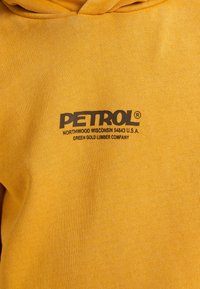 Felpa gialla in cotone con un logo nero "PETROL" ben visibile, accompagnato da un testo aggiuntivo sottostante e una finitura in tessuto testurizzato.