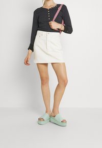 Marineblaues Langarmoberteil mit Knöpfen, weißer Denimrock und mintgrüne Plateausandalen. Das Oberteil hat ein strukturiertes Muster und schwarze Bündchen.