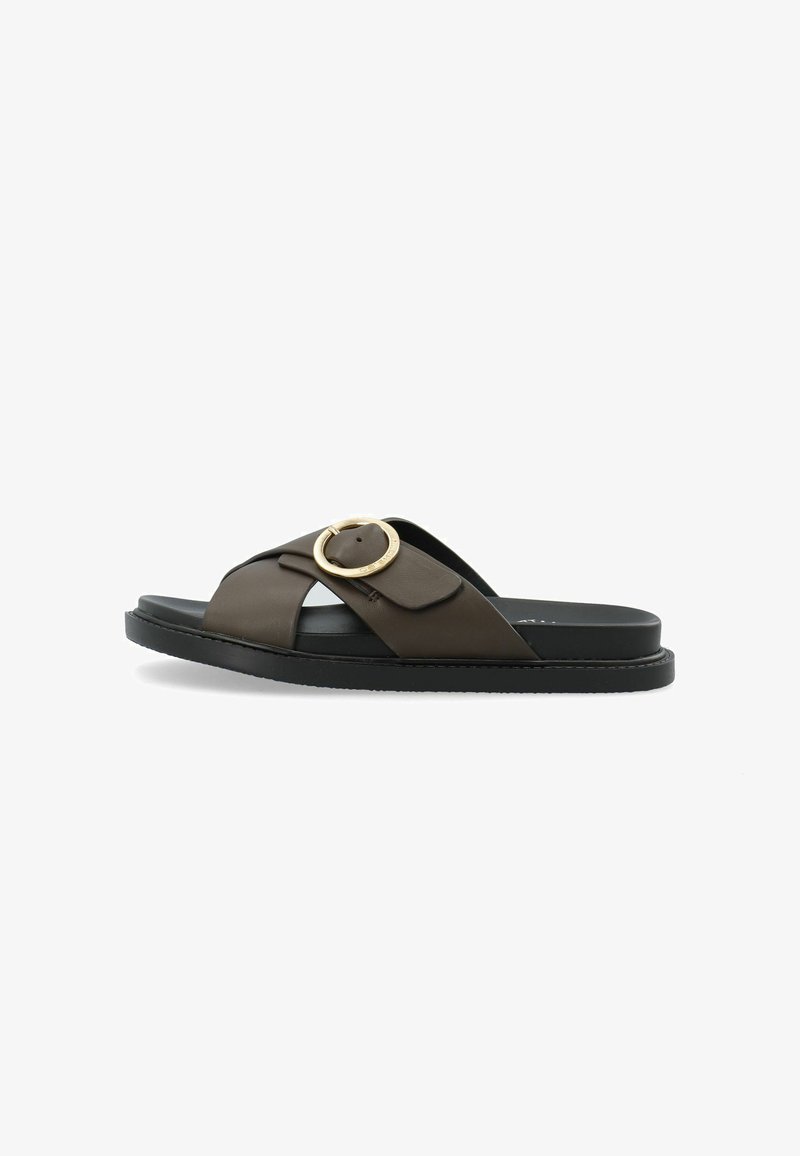 Sandaș cu talpă din piele maro, cu bretele încrucișate, accent auriu rotund și talpă din cauciuc negru. Design plat cu textură minimă.