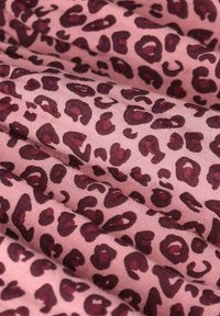 Le tissu à imprimé léopard présente des taches maroon foncé sur un fond rose doux, avec une texture lisse et une drape naturelle.