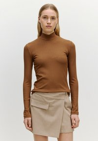Bruine geribbelde lange mouwen coltrui in combinatie met een beige wikkelrok met een voorkzak. Gladde textuur en aansluitend ontwerp.