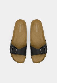 Paire de sandales à semelle beige avec des brides réglables noires à boucle et le logo "ANNA FIELD" imprimé sur les semelles, vues de dessus sur un fond blanc.