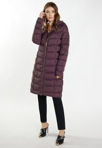 Dlhý fialový puffr kabát so zapínan�ím na zips a kapucňou, s prešívaným dizajnom. V spojení s čiernymi upravenými nohavicami a vysokými podpätkami.