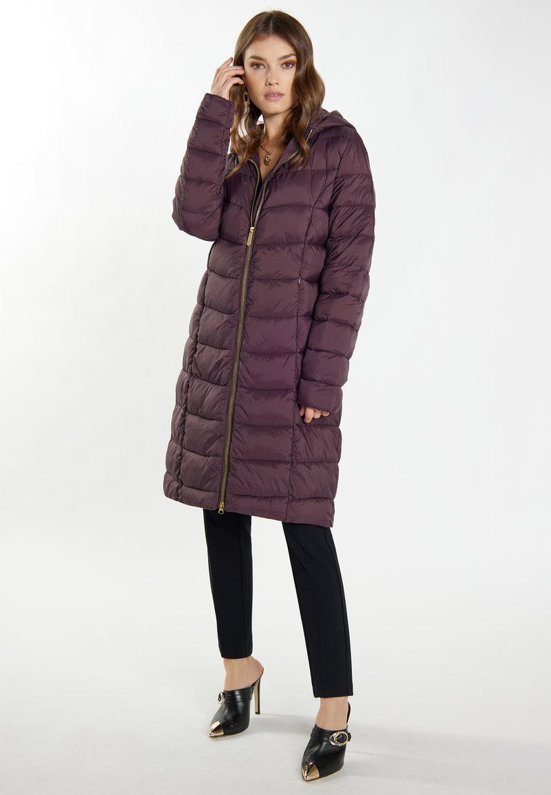 Dlhý fialový puffr kabát so zapínaním na zips a kapucňou, s prešívaným dizajnom. V spojení s čiernymi upravenými nohavicami a vysokými podpätkami.