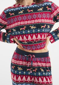 La ropa de casa de color rojo y azul marino con estampado presenta teckels, copos de nieve y árboles de Navidad, fabricada en una suave tela con una cinturilla elástica.