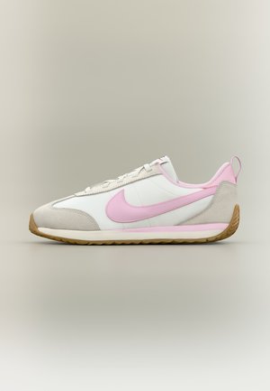 Zapatilla blanca y beige con el logotipo de Nike en rosa claro, lengüeta de talón rosa y suela de goma color caramelo, mostrada sobre fondo neutro.