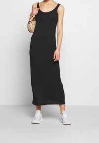 Czarna, bezrękawnikowa sukienka maxi o gładkiej teksturze, z okrągłym dekoltem. Połączona z białymi sportowymi trampkami i małą beżową torbą.