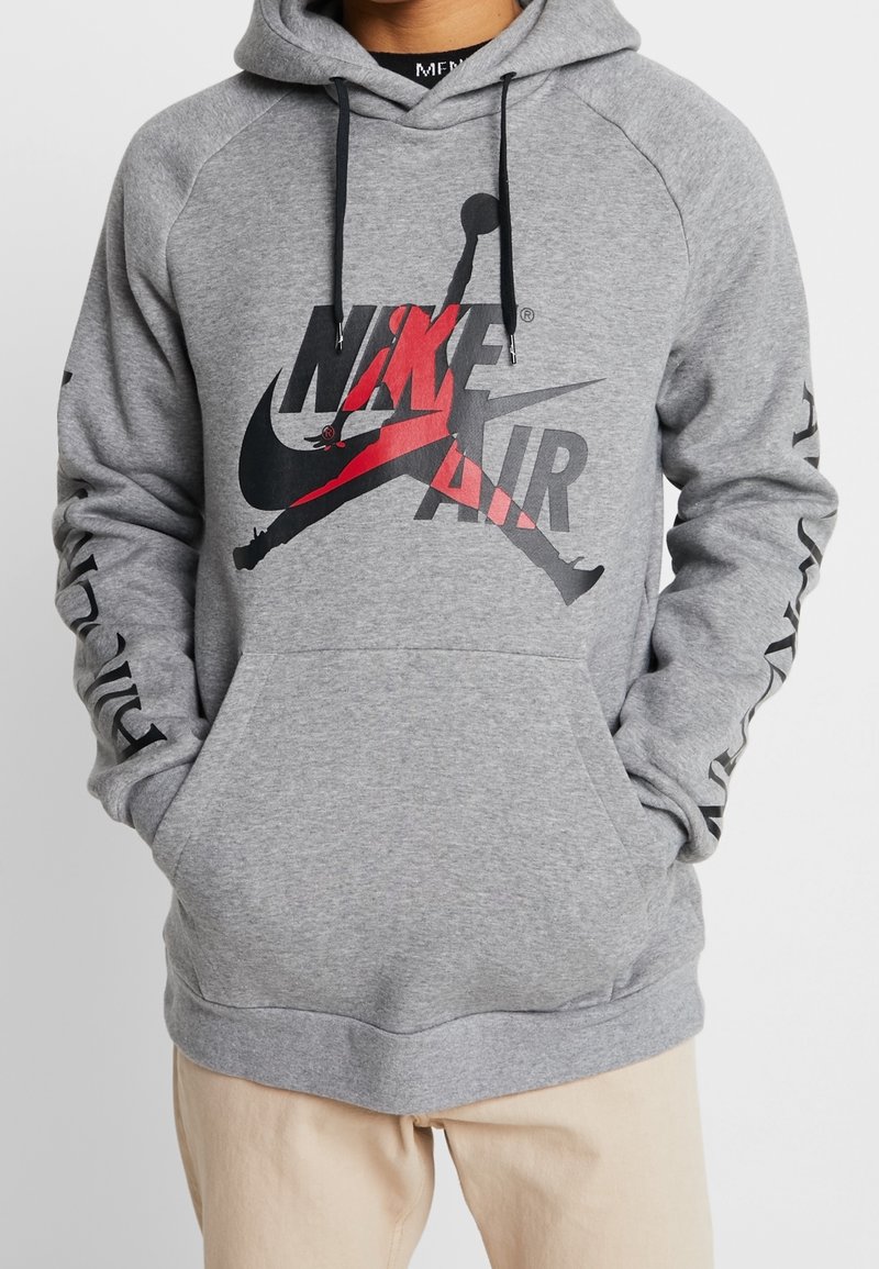 Sudadera gris con gráfico negro y rojo de "Nike Air". Cuenta con un bolsillo tipo canguro, capucha con cordones y detalles negros en las mangas.