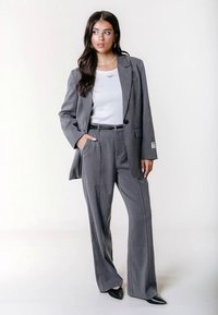 Siva obleka z ozkimi črtami, krojena blazer jakna in široke hlače. Kombinirana z belo majico in črnimi čevlji z ostrim prstom. Srebrni nakit za poudarek.