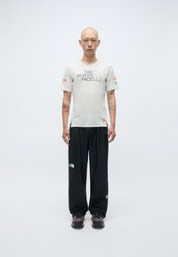 T-shirt de sport gris clair avec le logo "The North Face", associé à un pantalon noir ample et des chaussures robustes noires. Design simple, sans motifs.