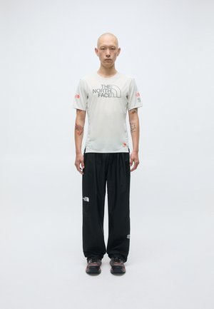 T-shirt de sport gris clair avec le logo "The North Face", associé à un pantalon noir ample et des chaussures robustes noires. Design simple, sans motifs.