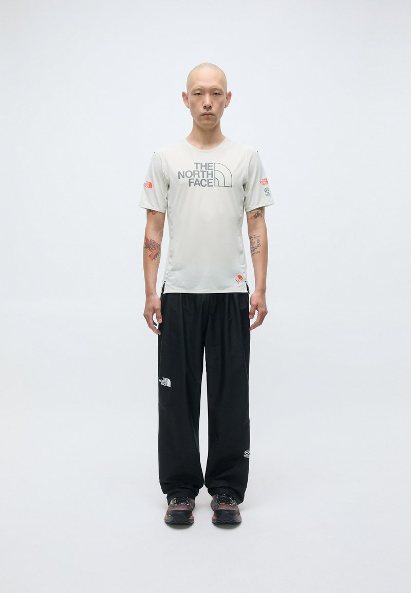 T-shirt de sport gris clair avec le logo "The North Face", associé à un pantalon noir ample et des chaussures robustes noires. Design simple, sans motifs.