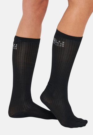 Black knee-high socks with vertical ribbed texture, featuring white printed numbers and letters on the upper side. Lightweight and semi-sheer design.