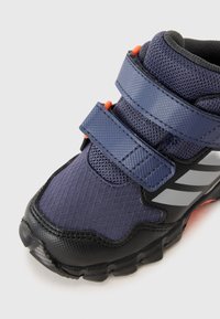 Bottines de sport bleu marine en matériau mesh et synthétique, dotées de bandes auto-agrippantes, d'accents noirs et de rayures réfléchissantes argentées.