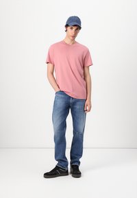 Camiseta de algodón rosa claro, de mangas cortas, con escote en forma de v; combinada con jeans de denim azul, con detalles desgastados, y zapatillas negras con acentos blancos.