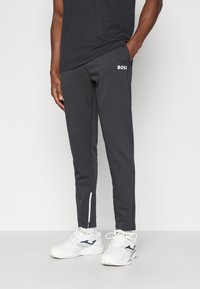 Μαύρο αθλητικό παντελόνι με λευκό λογότυπο "BOSS", σχέδιο tapered, με διακοσμητικά φερμουάρ στις πλευρές, κατασκευασμένο από λείο ύφασμα. Φοριέται με λευκά αθλητικά παπούτσια.