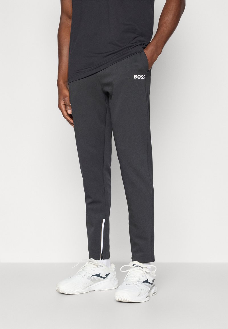 Μαύρο αθλητικό παντελόνι με λευκό λογότυπο "BOSS", σχέδιο tapered, με διακοσμητικά φερμουάρ στις πλευρές, κατασκευασμένο από λείο ύφασμα. Φοριέται με λευκά αθλητικά παπούτσια.