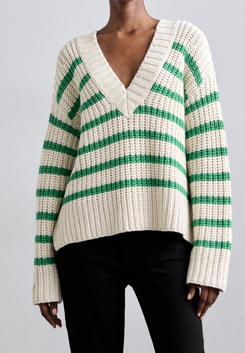 Pull en tricot à encolure en V, présentant des rayures alternées vertes et crème. Tissu texturé avec des manches larges et une coupe décontractée.