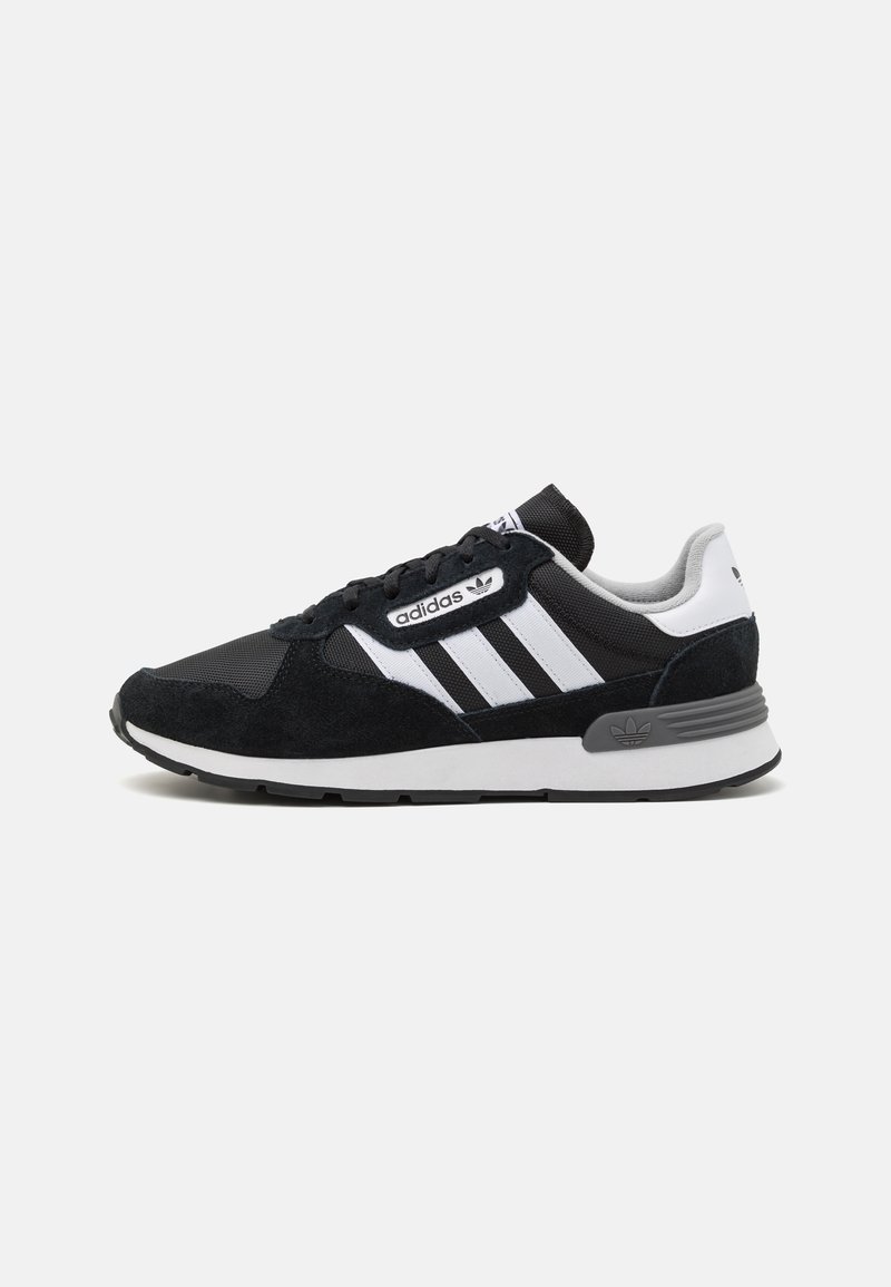Fekete és szürke sneakers, mely hálós és velúrból készült, három fehér csíkkal, fűzős rögzítéssel és texturált gumi talppal rendelkezik, melyen a saroknál márkázás található.