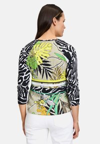 Multikleurige gebreide top met een zwart-wit zebrapatroon, tropische bladvormen in groen en geel, en contrasterende gestreepte accenten.