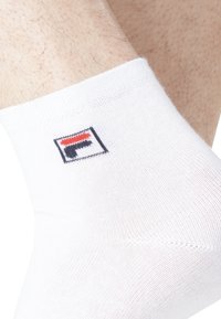 Chaussette de cheville blanche avec un tricot fin, ornée d'un petit logo bleu, rouge et blanc au niveau de la cheville. Design simple et fonctionnel.
