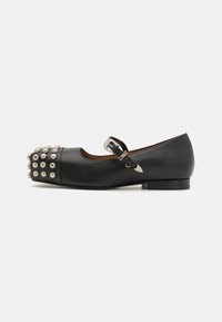 Zapato plano estilo Mary Jane de cuero negro con punta redonda, que presenta un adorno decorativo de tachuelas en la puntera y una correa con hebilla.