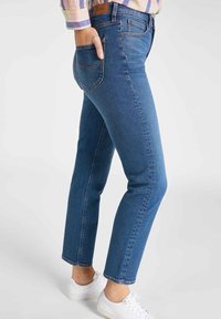 Jeans de denim azul con un corte recto, que cuentan con cinco bolsillos y un acabado sutilmente desgastado. Combinados con zapatillas blancas.