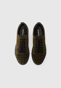 Gröna mockaskor med svarta skosnören, utrustade med en nitar-tåhuvud och en slät yta, designade för vardagsbruk.