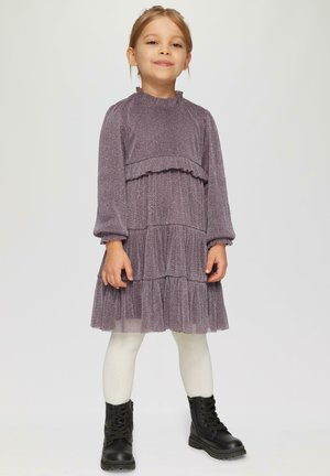Robe violette à plusieurs niveaux, avec des manches longues, un ourlet volanté et un tissu texturé. Portée avec des collants blancs et des bottes noires à lacets.