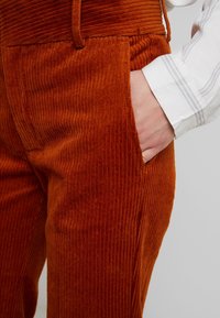 Cordhosen in einem satten Orangeton mit vertikalen Rippungen, ausgestattet mit seitlichen Taschen und einer hohen Taille.