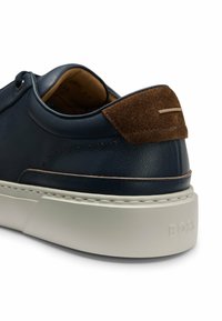 Navy nahkalentävät, joissa on ruskea mokka kantapään aksentti, valkoinen välipohja ja pieniä viiltoja sivuilla ilmanvaihtoa varten.