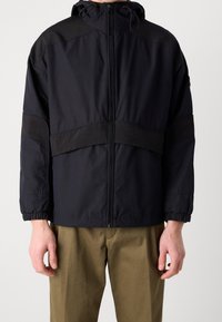 Černá bunda se zipem vpředu, nastavitelnou kapucí a elastickými manžetami. Vyznačuje se kontrastními matnými panely a elegantním, minimalistickým designem.