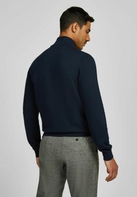 Marineblauw gebreid polo met een hoge kraag, met lange mouwen. Gepaard met lichtgrijze, textuuroverhemdbroek met subtiele patroondetails.