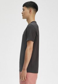 T-shirt grigio scuro a maniche corte in tessuto di cotone, con scollatura rotonda e taglio dritto. Indossato con pantaloni corti rosa chiaro, visto di lato.