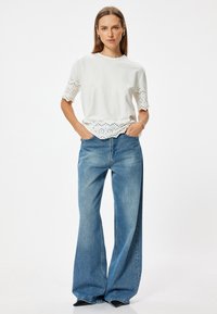 Camiseta de algodón blanca con diseño de ojales en las mangas y el dobladillo, combinada con unos vaqueros de pierna ancha de color azul claro, que presentan un ajuste clásico de cintura alta.