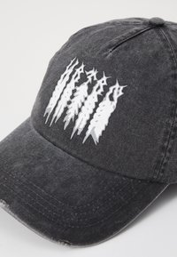 Cap din denim negru cu brăcătură curbată și detalii ușor uzate, având un design grafic alb cu urme de gheare pe panoul frontal.