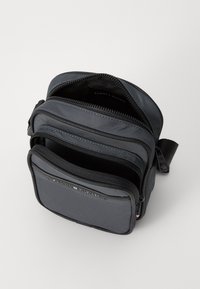 Borsa a tracolla nera in nylon con più scomparti con zip, tracolla regolabile e un'accenno di logo sul davanti. Texture liscia, design compatto.