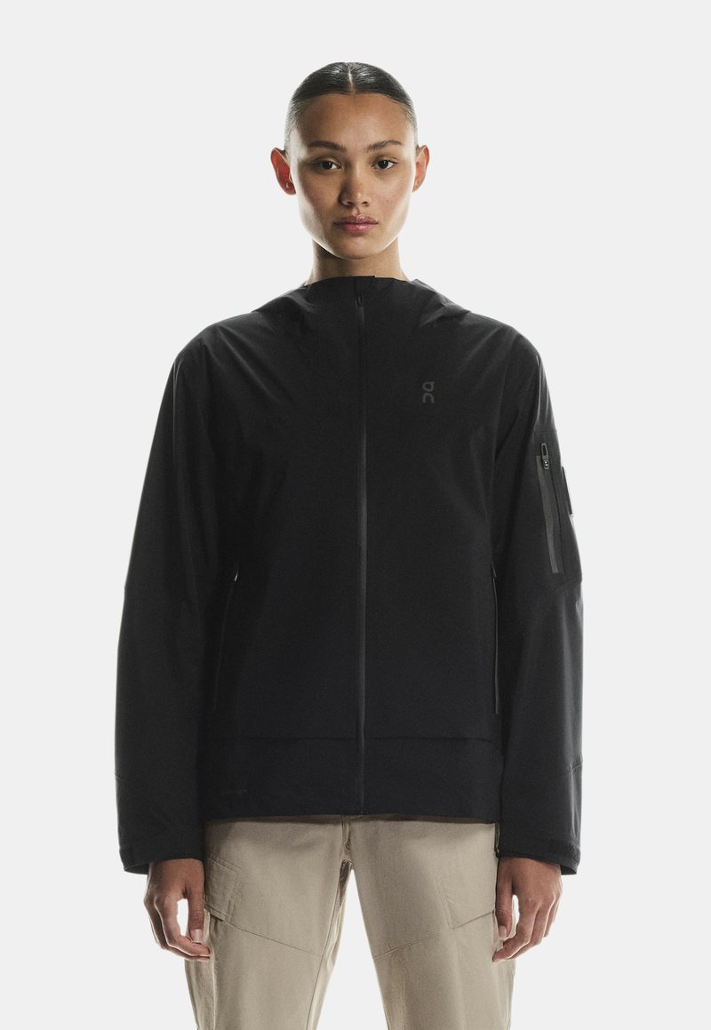 Czarna kurtka na zamek z kapturem. Gładka tekstura, lekko luźny krój, z kieszenią na zamek na lewym ramieniu i detalem z logo.