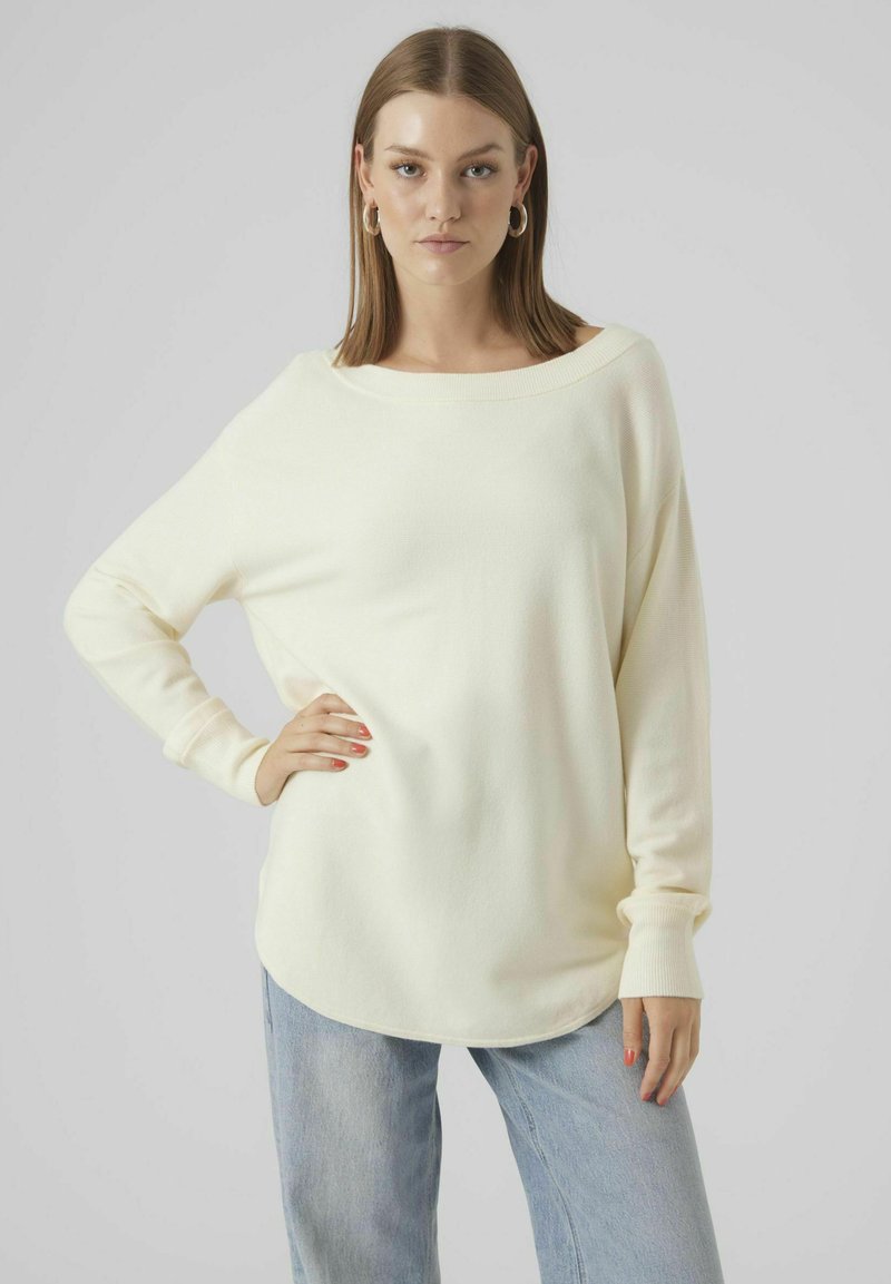 Cremefarbener Langarmpullover mit weitem Ausschnitt, weichem Material und lässiger Passform. Kombiniert mit hellblauen, locker sitzenden Jeans.