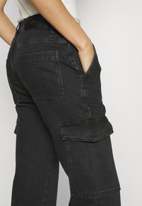 Zwarte denim cargobroek met een losse pasvorm, voorzien van zijzakken, achterzakken en contrasterende stiksels. Soepele textuur.