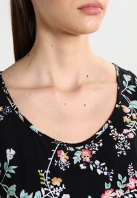 Musta kukkamekko, jossa on pyöreä pääntie, värikkäät kukkakuviot, sileä kangas ja lyhyet hihat. Yksityiskohtina vaihtelevat kukkien värit.