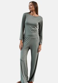 Zestaw odzieży loungewear w jasnym oliwkowym kolorze, składający się z długiego rękawa bluzki z dekoltem typu łódka oraz spodni o szerokich nogawkach, wykonany z miękkiej, elastycznej tkaniny.