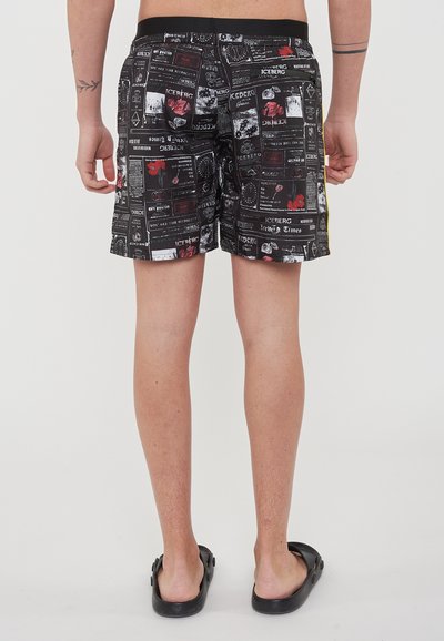 Costume da bagno neri con vari stampati grafici bianchi e rossi. Fodera in rete e vita elasticizzata, con una striscia laterale gialla.