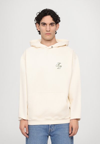Cream-colored hoodie with a front pocket, drawstring hood, and embroidered logo in green. Slim-fit design with long sleeves.