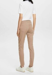 Beige slim-fit-housut, joissa on takataskut, yhdistetty valkoiseen t-paitaan ja valkoisiin lenkkareihin. Sileä kangas, joka muistuttaa puuvillaa.